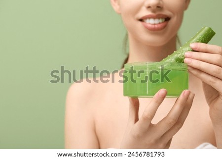 Beautiful young woman with aloe vera leaf in jar of facial gel on green background