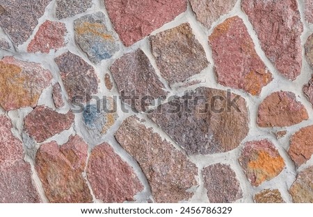 It's close up view of the colorful wall. Its photo of multicolor stonewall. It is photo of multicolored srone wall. its view of red sidewalk. It's the view of mosaic stonewall
