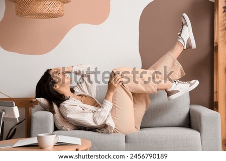 Young woman lying on grey sofa at home Royalty-Free Stock Photo #2456790189