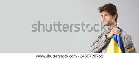 Young male Ukrainian soldier with flag on grey background with space for text