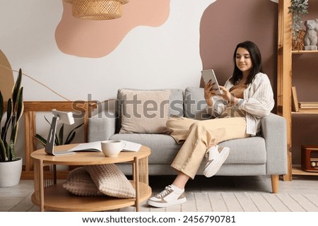Young woman using tablet computer on grey sofa at home Royalty-Free Stock Photo #2456790781