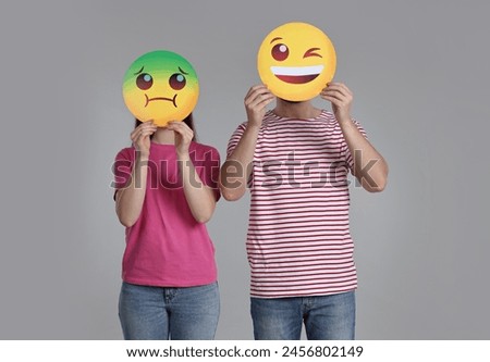 People covering faces with emoticons on grey background