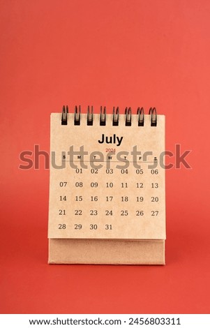 July 2024 white mini desk calendar on red color background.