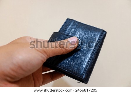 Man hand holding black wallet isolated on cream background, finance, stock photo. 