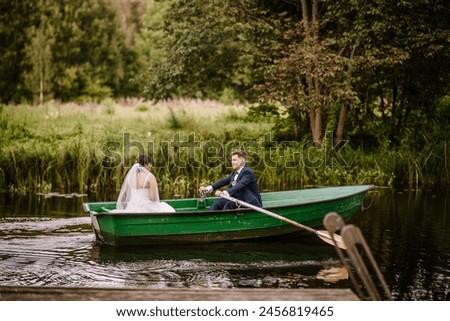 Valmiera, Latvia - August 19, 2023 -  a bride and groom in a green rowboat on a river, with lush greenery in the background. The groom is rowing the boat.