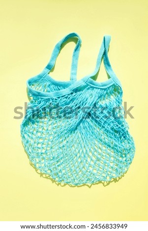 Reusable blue mesh bag on a yellow background in sunny daylight. Mesh shopping bags. Sustainable use concept