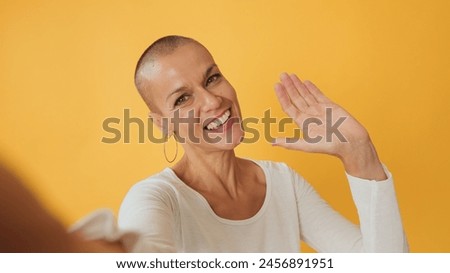 Close-up, young hairless woman ooking at camera making video call, welcome sign, isolated on yellow background in studio