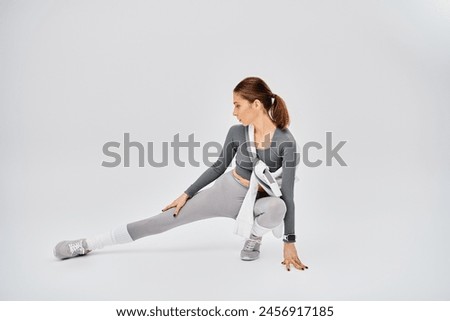 Sporty young woman in active wear gracefully stretches her body on a grey background.