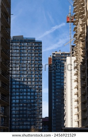 Residential multi-storey buildings and high-rise buildings under construction with a construction crane in the foreground on a sunny day. Concept of construction, urbanization. Vertical photo