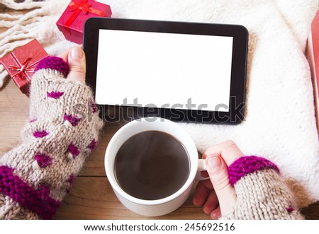 Female Hands Holding a Tablet and a Coffee Cup with Christmas Gifts Near