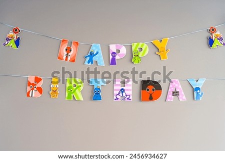 Paper sign Happy Birthday with colorful monsters from virtual games on a gray background