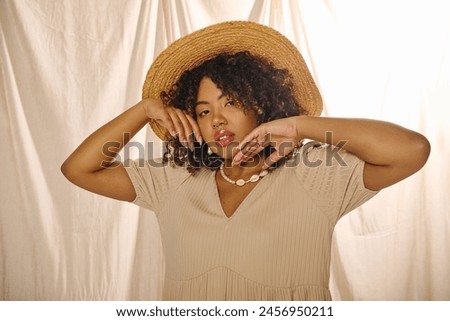 A beautiful young African American woman with curly hair wearing a straw hat and summer dress poses gracefully for a picture.