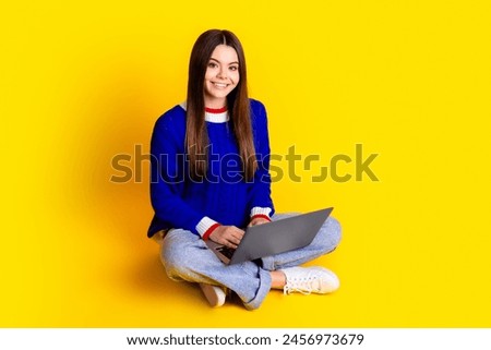 Full length photo of pretty teen girl hold netbook crossed legs wear trendy knitwear blue outfit isolated on yellow color background
