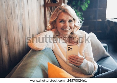 Photo portrait of lovely retired woman sit sofa hold gadget dressed casual outfit cozy home interior living room in brown warm color
