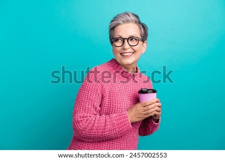 Portrait of cheerful senior woman in glasses hold cappuccino look at coffee shop logo empty space isolated on turquoise color background Royalty-Free Stock Photo #2457002553