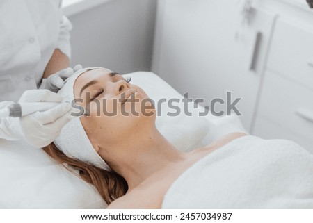 Beautician uses RF lifting to improve skin tone and tighten contour face. This safe and effective method uses radio frequency waves to stimulate collagen and elastin, improving skin structure and Royalty-Free Stock Photo #2457034987