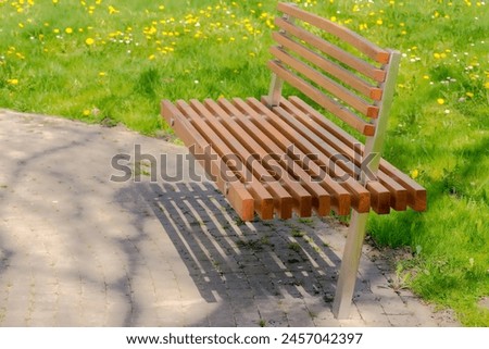 A park bench by the lawn . A stainless steel and wood bench on a cobblestone path at the edge of the lawn. 