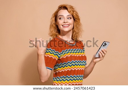 Portrait of nice girl with wavy hair wear t-shirt hold smartphone look directing at sale empty space isolated on beige color background