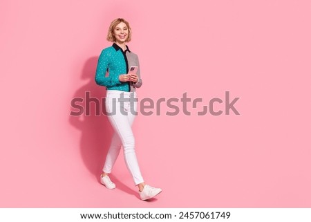 Full size photo of pretty young girl walking hold device wear trendy striped cyan outfit isolated on pink color background