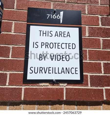 Clear warning on a black and white sign stating 'This area is protected by video surveillance', affixed to a brick wall to enhance security.
