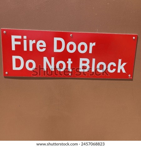 Vivid red sign stating "Fire Door Do Not Block", prominently mounted on a wall to enforce safety regulations and ensure unobstructed access in emergencies.
