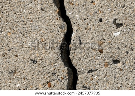 A crack in the pavement with rocks and debris in it. The crack is wide and deep, and the rocks are scattered all over the ground. Scene is one of destruction and decay