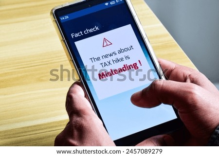 Mobile phone with fact check fake news alert on a tax hike report. Misleading, disinformation biased news, concept. Royalty-Free Stock Photo #2457089279