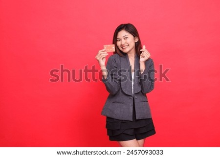 Asian businesswoman expression happy sign of love (saranghaeyo) and holding debit credit card wearing jacket and skirt on red background. for financial, business and advertising concepts