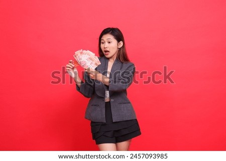gesture of asian office girl surprised candid both hands holding credit card and money wearing jacket and skirt on red background. for financial, business and advertising concepts