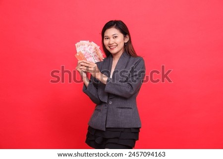 Cheerful Asian girl director's expression with both hands holding credit, debit and money cards at the camera wearing a gray jacket and red skirt. for transaction, business and advertising concepts