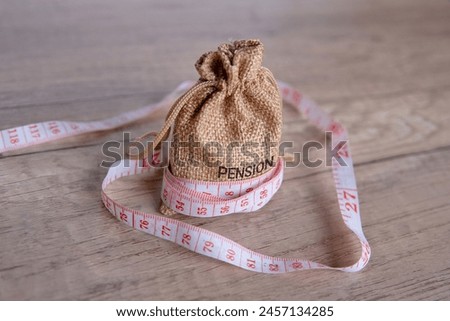 Money bag with word PENSION and tape measure. Retirement, low pension, poverty concept. Royalty-Free Stock Photo #2457134285