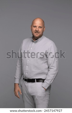 A studio portrait of a bald man in a light grey shirt, looking directly at the camera with a slight smile.