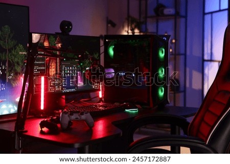 Playing video games. Stylish room interior with modern computer, wireless controllers and gaming chair in neon lights