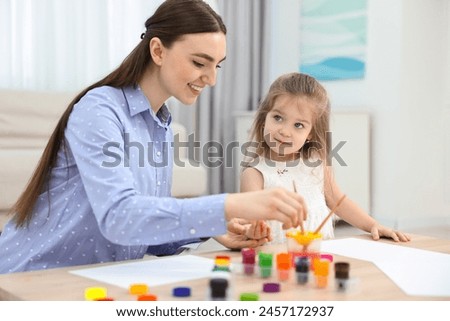 Mother and her little daughter painting with palms at home