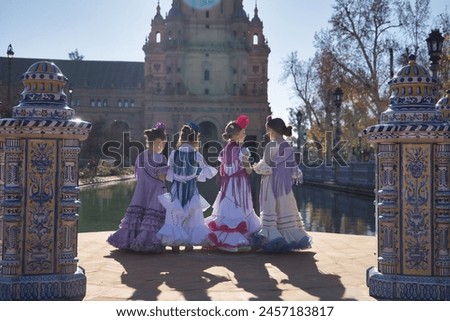 Four girls dancing flamenco, with their backs turned and talking to each other, in typical flamenco costumes next to a lake in a beautiful square in Seville. Concept dance, flamenco, typical Spanish. Royalty-Free Stock Photo #2457183817