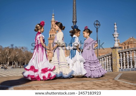 Four girls dancing flamenco, talking to each other, in typical flamenco costumes on a bridge in a beautiful square in Seville. Dance concept, flamenco, typical Spanish, Seville, Spain. Royalty-Free Stock Photo #2457183923
