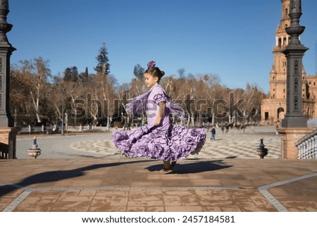 Girl dancing flamenco, twirling to show off her costume, in typical flamenco dress on a bridge in a beautiful square in Seville. Dance concept, flamenco, typical Spanish, Seville, Spain. Royalty-Free Stock Photo #2457184581
