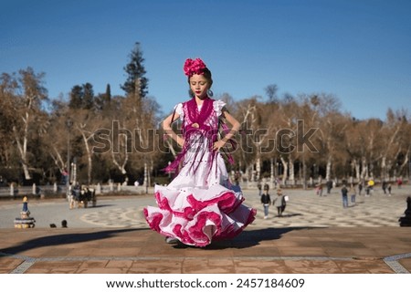 Girl dancing flamenco, posing looking at camera, in typical flamenco dress on a bridge in a nice square in Seville. Dance concept, flamenco, typical Spanish, Seville, Spain. Royalty-Free Stock Photo #2457184609