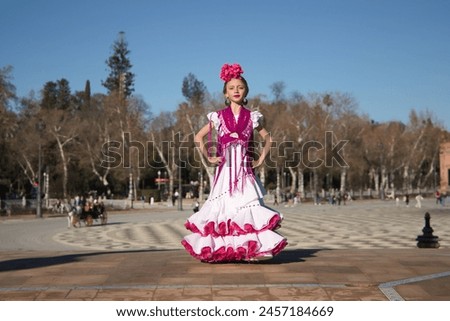 Girl dancing flamenco, posing looking at camera, in typical flamenco dress on a bridge in a nice square in Seville. Dance concept, flamenco, typical Spanish, Seville, Spain. Royalty-Free Stock Photo #2457184669
