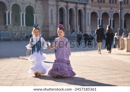 Two girls dancing flamenco walking and talking happily, with typical flamenco dress in a nice square in Seville. Dance concept, flamenco, typical Spanish, Seville, Spain. Royalty-Free Stock Photo #2457185361