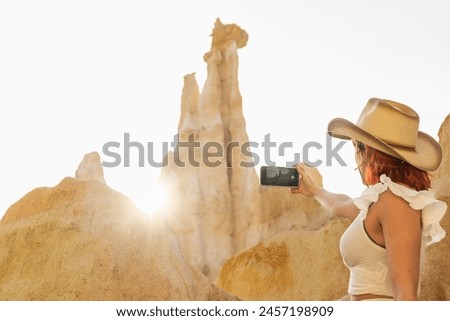 A woman is taking a picture of a mountain with a cell phone. The photo has a mood of adventure and exploration