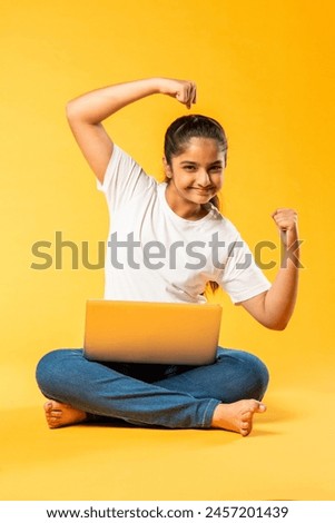 Indian asian pretty small school girl using laptop sitting isolated on yellow background