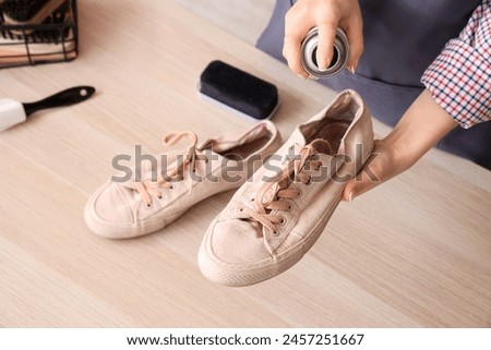 Female shoemaker applying water repellent spray over pair of gumshoes at wooden table, closeup Royalty-Free Stock Photo #2457251667