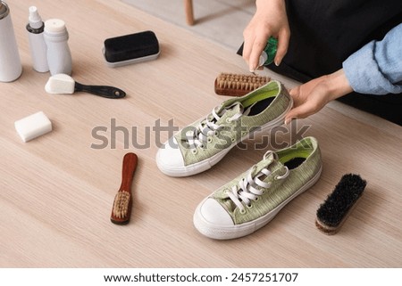 Female shoemaker with stylish gumshoes and cleaning supplies at wooden table Royalty-Free Stock Photo #2457251707