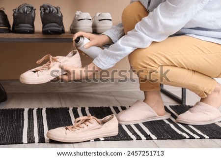 Woman applying water repellent spray on gumshoes at home Royalty-Free Stock Photo #2457251713