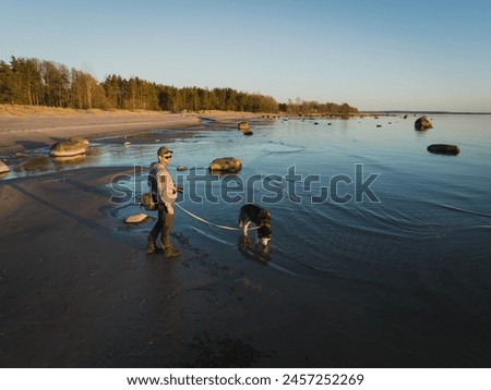 A guy landscape photographer with a husky dog ??stands on the beach at sunset, photo from a drone. 