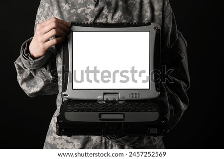 Soldier in uniform holding military laptop with blank screen on black background