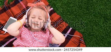 Cute little girl listening to music on plaid outdoors. Banner for design