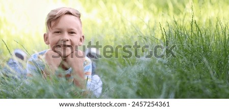 Cute little boy lying on green grass outdoors. Banner for design