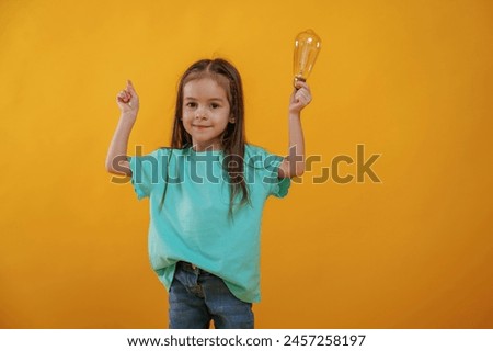 Having an idea, holding light bulb. Cute little girl is against yellow background.